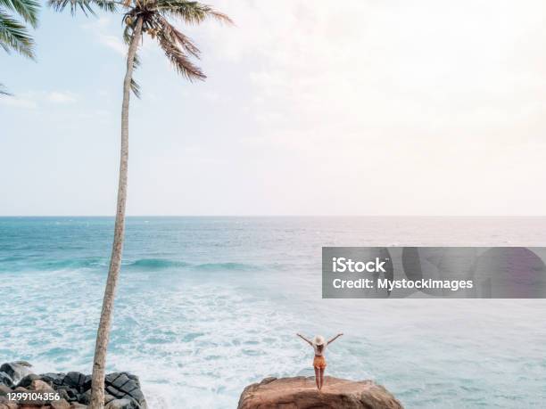 Woman On Rock Above Sea Stands Arms Out Wide Stock Photo - Download Image Now - Aura, Beach, Summer