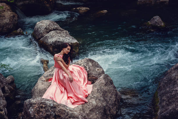 River witch, sitting on a rock in river. Pink long dress, a fabulous image.Fashionable toning. Creative color. River witch, sitting on a rock in river. Pink long dress, a fabulous image.Fashionable toning. Creative color. Beautiful dancer in a mystical forest by the river dark pink dress stock pictures, royalty-free photos & images