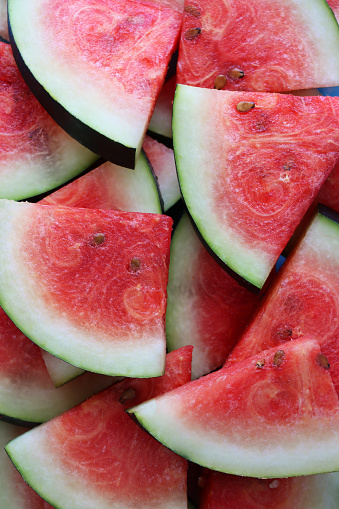 Photo showing a close-up, elevated view of pile of watermelon slices, which have been cut into pie-shaped wedges.