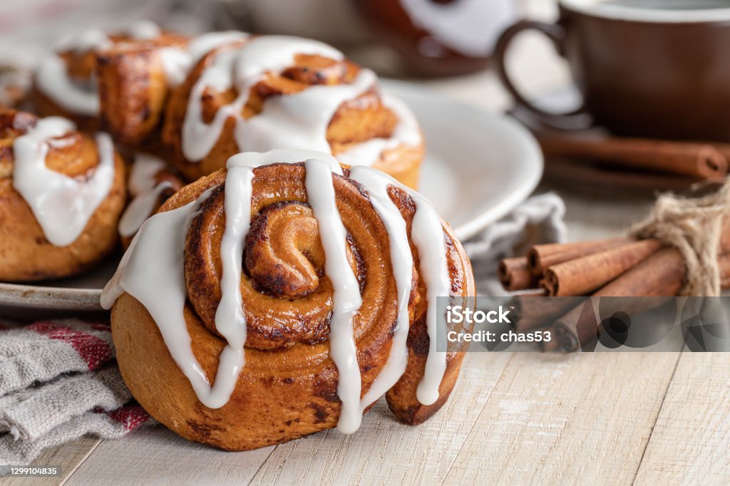 Cinnamon Roll With White Icing Closeup of a baked cinnamon roll with white icing on a wooden table Cinnamon Bun Stock Photo