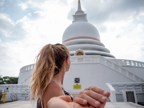 Couple holding hands woman leading the way to beautiful white temple in Sri Lanka. Buddhist Japanese peace pagoda. People travel together sharing moments
