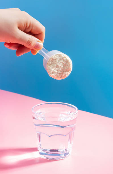 weibliche hand gießt proteinpulver in glas wasser auf blaurosa hintergrund. - dieting front view vertical lifestyles stock-fotos und bilder