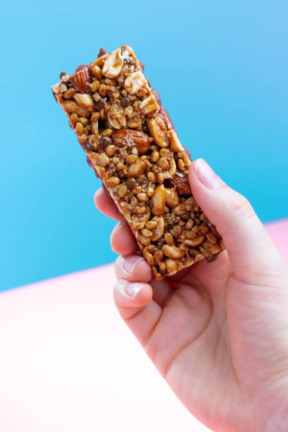 istock Female hand holding a protein bar on blue and pink background. 1299105649