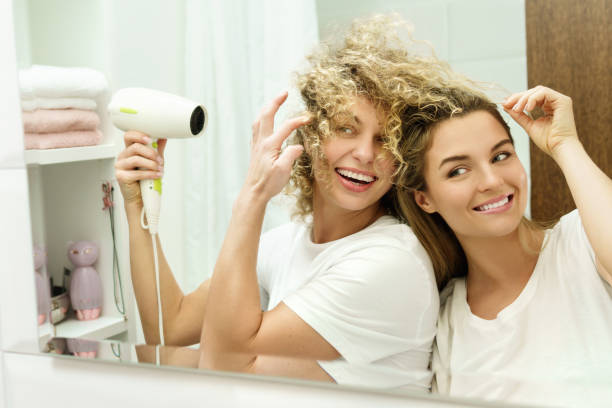 две молодые и веселые женщины с помощью фена - hair care human hair women blond hair стоковые фото и изображения