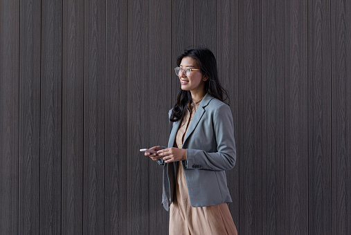 Elegant Asian businesswoman using her smartphone outdoors (grey wooden background)