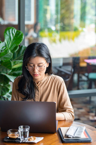 istock Asian Woman/College Student Using a Laptop Computer to Study Remotely at a Cafe 1299107329
