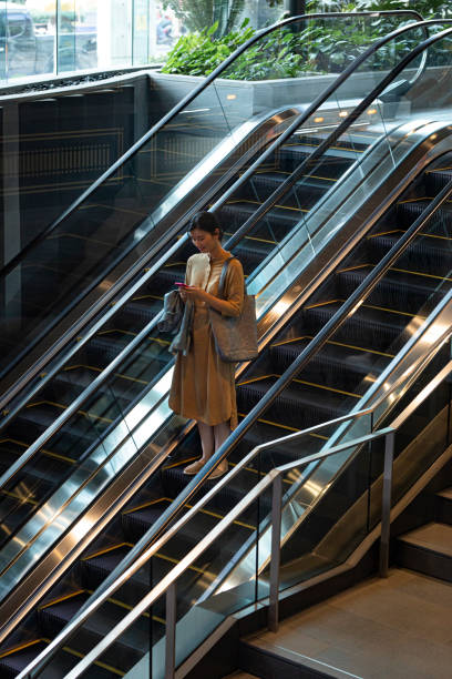 istock Asian Woman With a Smartphone Riding on an Escalator 1299107383