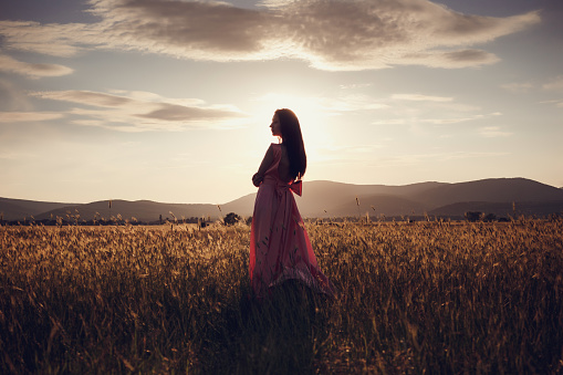 beautiful woman walking on wheat field before sunset. Cute lady walking through the meadow.