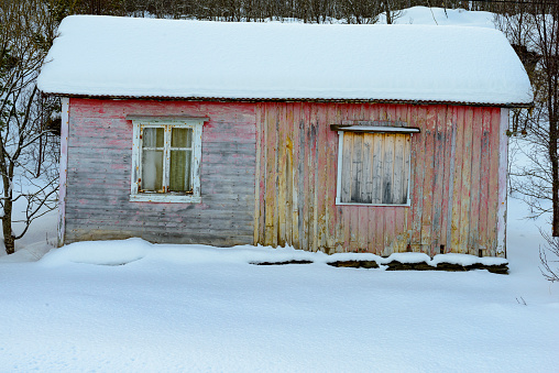 Abandoned old wooden shed with faded paint an damaged wood in a snowy winter forest in Northern Norway during winter.