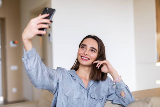 istock Young woman at home indoors lying on a sofa and taking a selfie by camera 1299113994