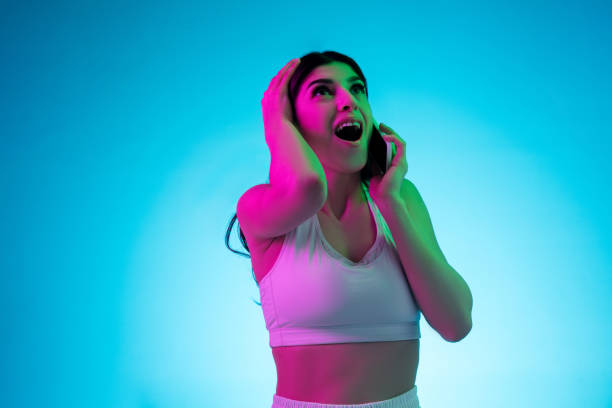 istock Brunette beautiful woman's portrait isolated on blue studio background in multicolored neon light. Talking phone. 1299115119