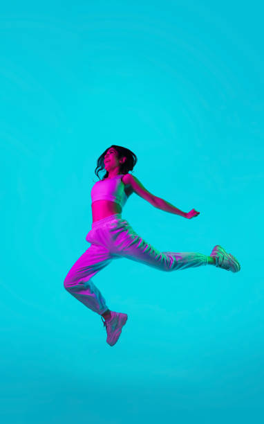 istock Brunette beautiful woman's portrait isolated on blue studio background in multicolored neon light. Jumping high. flying 1299116131