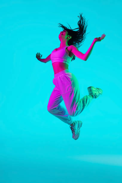 istock Brunette beautiful woman's portrait isolated on blue studio background in multicolored neon light. Jumping high. flying 1299116133