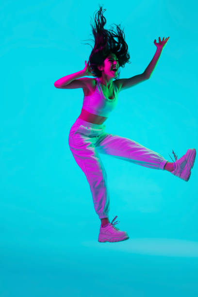 Brunette beautiful woman's portrait isolated on blue studio background in multicolored neon light. Jumping high. flying
