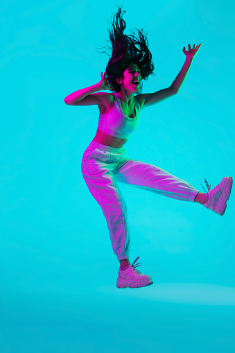 Crazy. Brunette woman's portrait on blue studio background in mixed neon. Beautiful model jumping high, flying with hair blowed out. Concept of human emotions, facial expression, sales, ad, fashion.