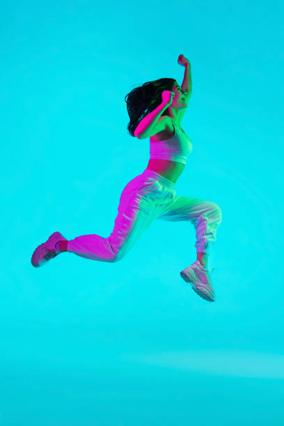 istock Brunette beautiful woman's portrait isolated on blue studio background in multicolored neon light. Jumping high. flying 1299116138