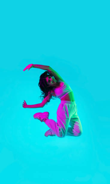 istock Brunette beautiful woman's portrait isolated on blue studio background in multicolored neon light. Jumping high. flying 1299116139