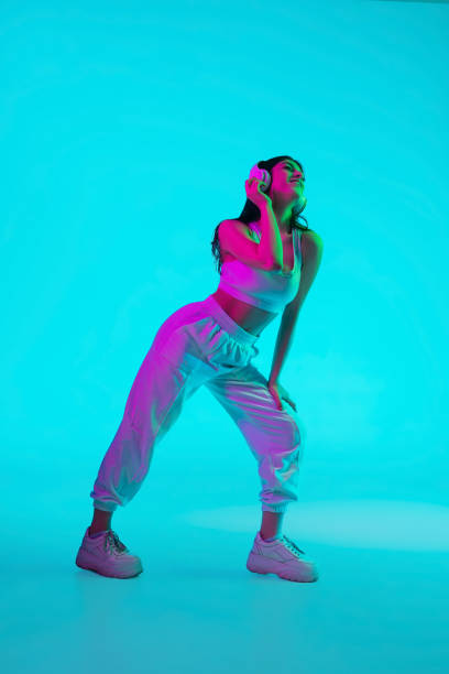 istock Brunette beautiful woman's portrait isolated on blue studio background in multicolored neon light. Dancing with headphones 1299116140