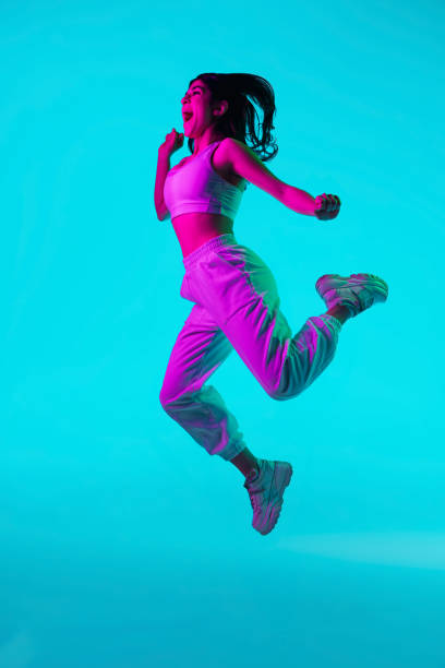 istock Brunette beautiful woman's portrait isolated on blue studio background in multicolored neon light. Jumping high. flying 1299116142