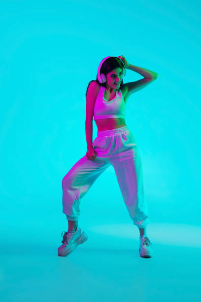 istock Brunette beautiful woman's portrait isolated on blue studio background in multicolored neon light. Dancing with headphones 1299116143
