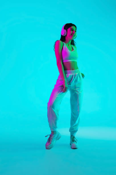 istock Brunette beautiful woman's portrait isolated on blue studio background in multicolored neon light. Dancing with headphones 1299116144