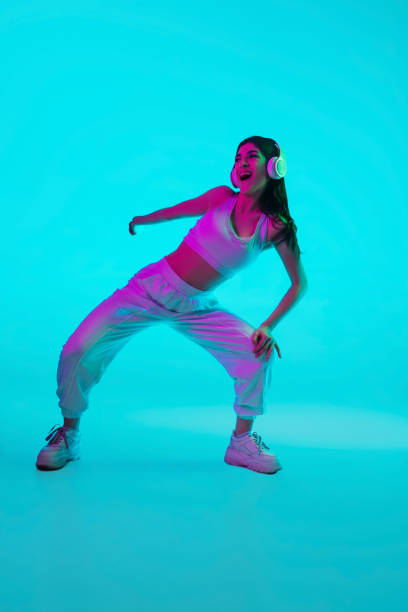 istock Brunette beautiful woman's portrait isolated on blue studio background in multicolored neon light. Dancing with headphones 1299116152