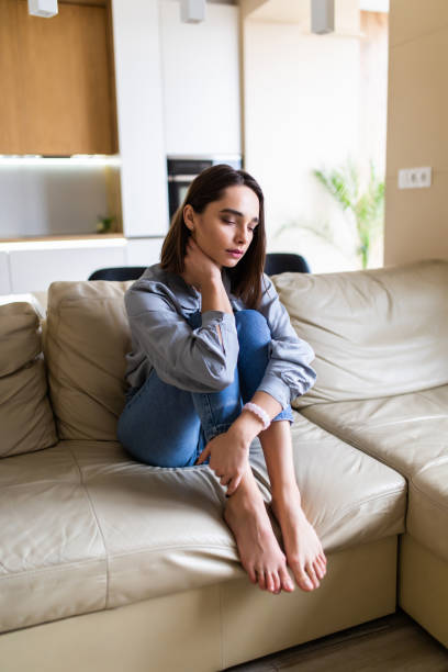 istock Sad young woman sitting on a sofa at home 1299116372