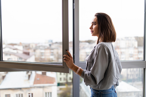 Young woman opening window in living room