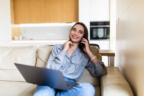 istock Young woman using laptop and cellphone on sofa at home 1299116538