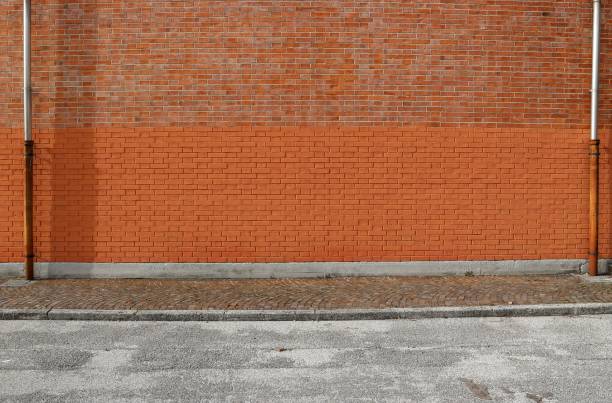 istock Bicolor brick wall with two gutters at the ends. Porphyry sidewalk and paved road in front. 1299119436