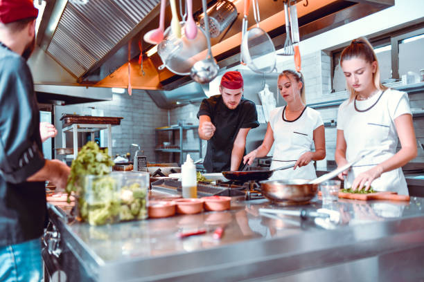 istock Male Cook Spicing Up Recipe While Female Colleagues Prepare It 1299124071