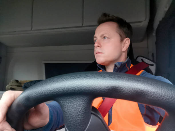 Truck Driver Wearing a High Vis Vest and Red Seat Belt view from the front with the Driver looking Right Truck Driver Wearing a High Visibility Vest and Red Seat Belt view from the front with the Driver looking Right with the interior of the Semi Truck Lockers behind. car point of view stock pictures, royalty-free photos & images