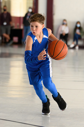 Young child (boy) athlete playing basketball in a youth football game