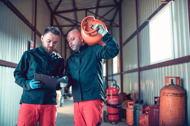 two male workers checking schedule in liquified gas store while carrying cylinder - liquified petroleum gas imagens e fotografias de stock