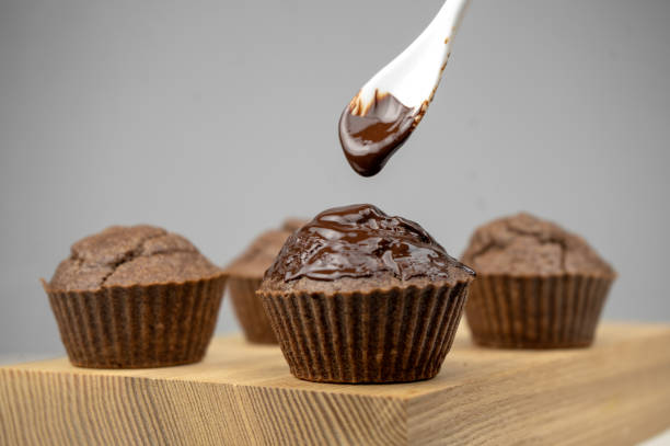 istock Pouring melted chocolate to chocolate brown muffins on wooden board 1299128420