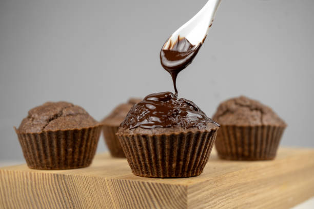 istock Pouring melted chocolate to chocolate brown muffins on wooden board 1299128435