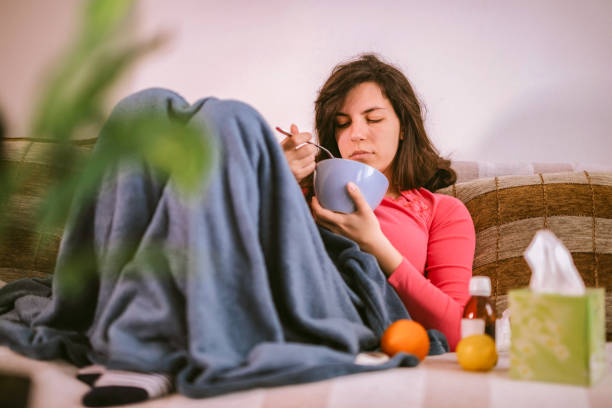 Down With The Flu Young Caucasian woman lying at home struck with a flu or seasonal cold. chicken soup stock pictures, royalty-free photos & images