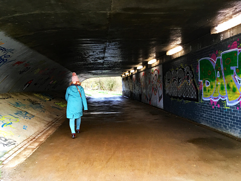 Reading, Berkshire, England, January 28th. 2021: Woman in a Blue Coloured Coat Walking in a Graffiti Covered Underpass