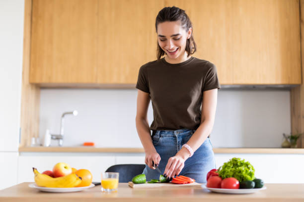 istock Young pretty woman cutting vegetables in kitchen at home 1299130443