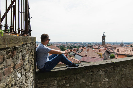 Young man sits from behind and looks at European old city from top. Lifestyle. Tourism and travel concept.