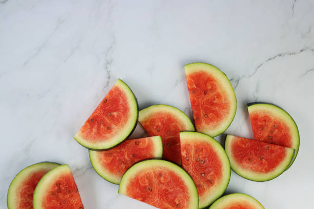 istock Image of watermelon slices / chunks pile, cut into semi-circles, grey and white marble effect background, copy space, elevated view 1299131679