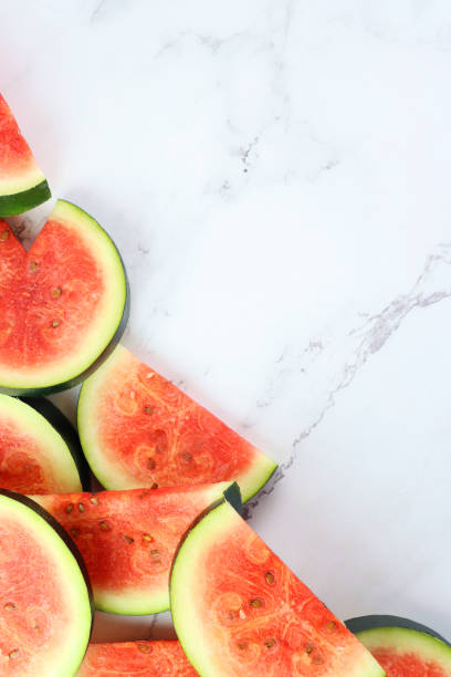 istock Image of watermelon slices / chunks pile, cut into semi-circles, grey and white marble effect background, copy space, elevated view 1299131717