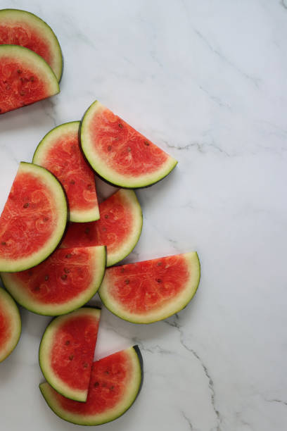 istock Image of watermelon slices / chunks pile, cut into semi-circles, grey and white marble effect background, copy space, elevated view 1299131759
