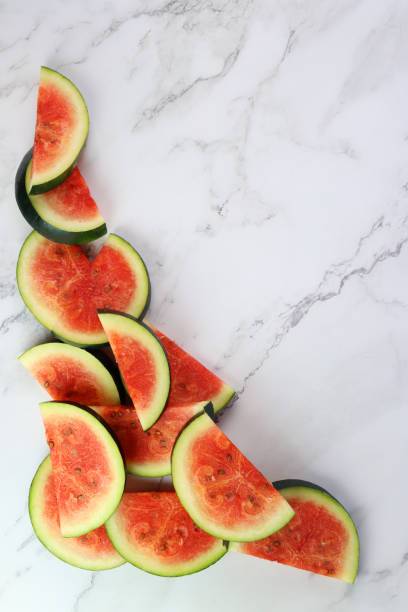 istock Image of watermelon slices / chunks pile, cut into semi-circles, grey and white marble effect background, copy space, elevated view 1299131794