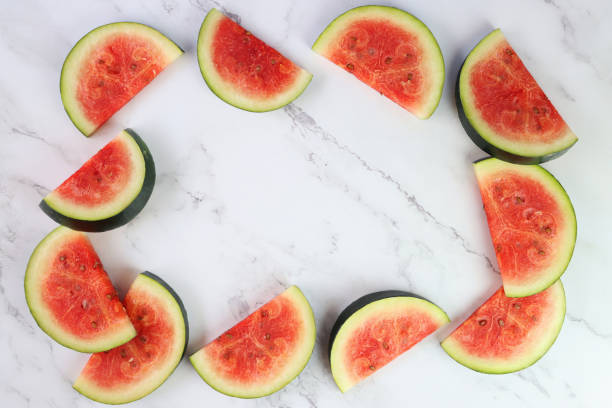 istock Image of watermelon slices / chunks frame, cut into semi-circles, grey and white marble effect background, copy space, elevated view 1299131820
