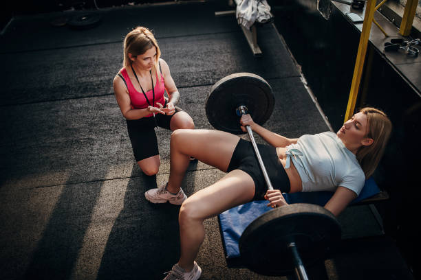 istock Female personal trainer watching young woman train with weights 1299131919