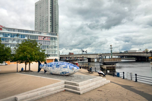 UK - Northern Ireland - Belfast - The blue and white ceramic Big Fish sculpture on the river Lagan public waterfront of Donegall quay with Obel tower and Dargan bridge at background