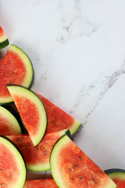 istock Image of watermelon slices / chunks pile, cut into semi-circles, grey and white marble effect background, copy space, elevated view 1299132123