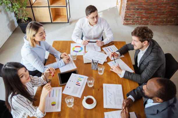 istock Diverse group of co-workers having casual discussion in office. Executives during friendly discussion, month reporting, creative meeting. Top view. 1299132924