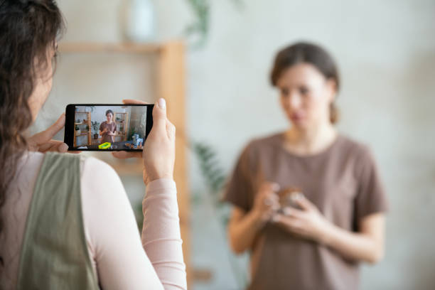 istock Young woman holding smartphone while shooting female with small bowl 1299133011